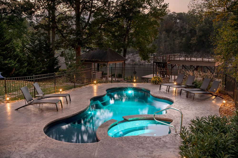Modern Freeform Fiberglass Pool with spa surrounded by a patio and deck furniture with a pond in the background