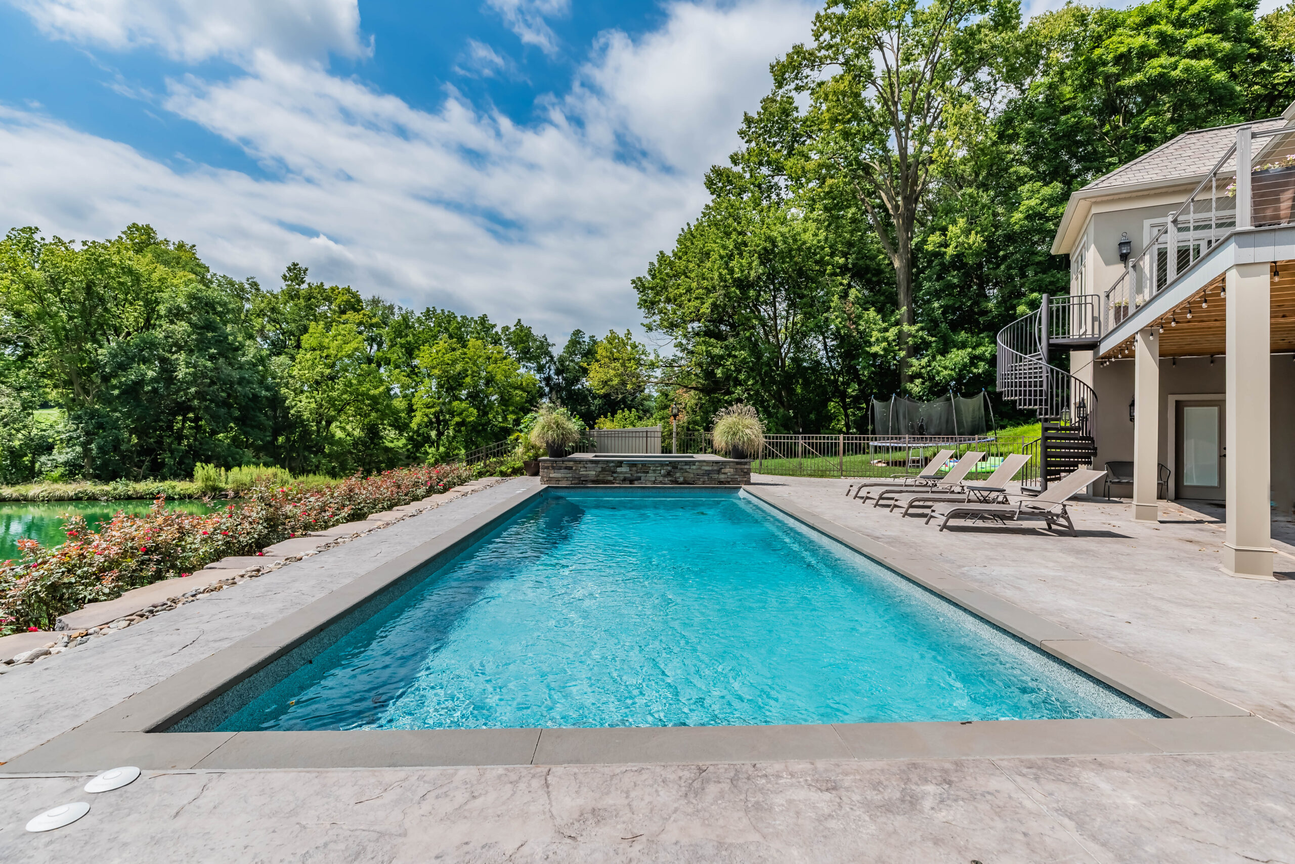Large rectangular fiberglass pool with outdoor seating on a sunny day