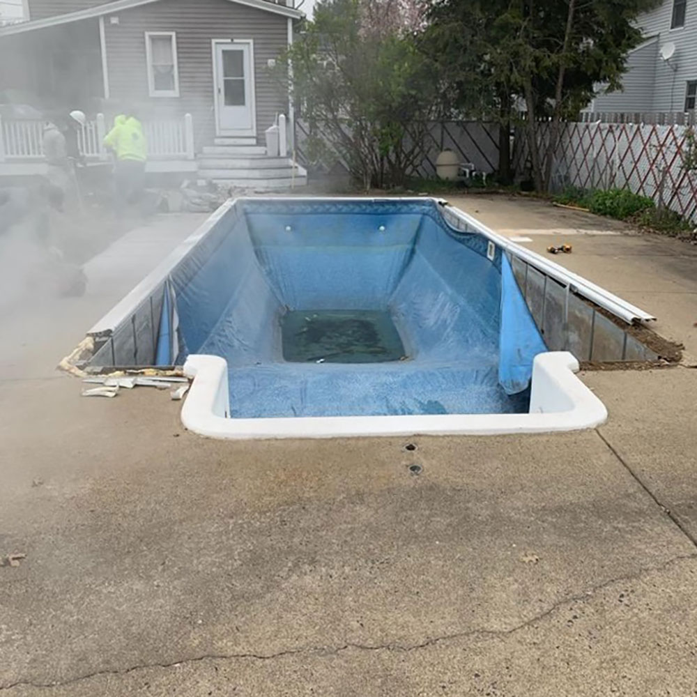 Rectangle vinyl liner pool with broken liner and concrete ground surrounding it