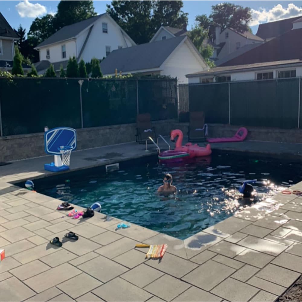 A square pool with tiled decking, pool toys and a child swimming