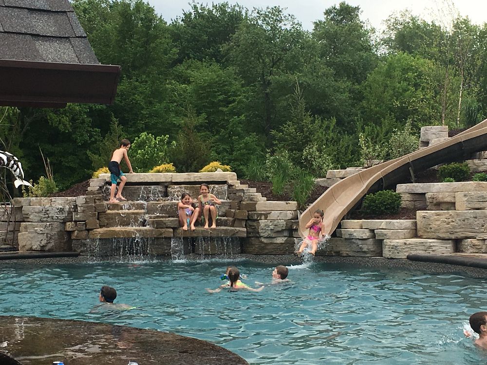 A pool with kids playing in it, including a water slide and waterfall