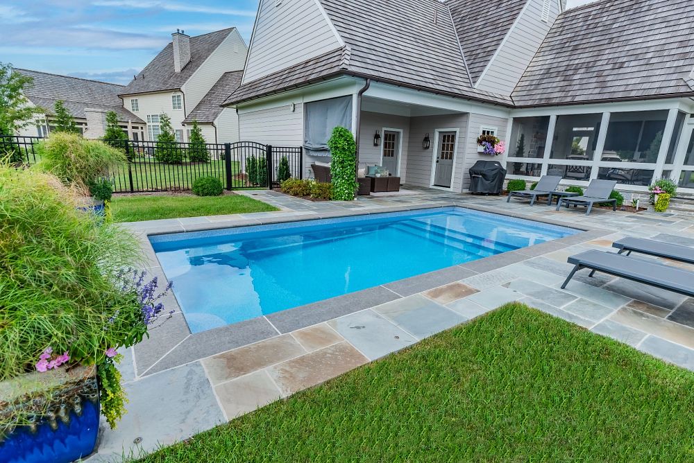 rectangular pool in small backyard with stone pavers and patio furniture