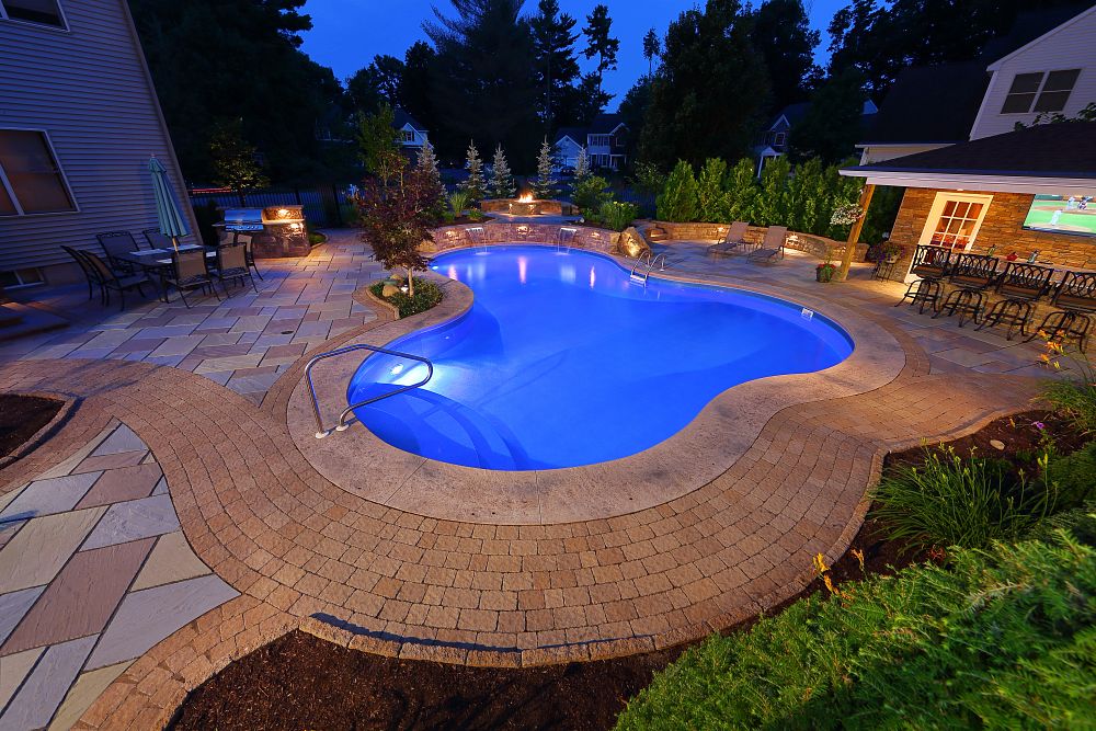 Curved vinyl liner pool in the evening, with in-pool lighting and stamped concrete decking