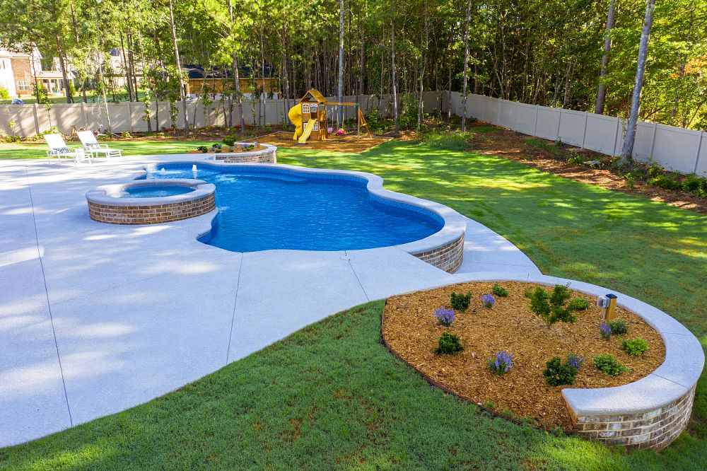 small free form pool with spa surrounded by a patio and lush backyard and trees