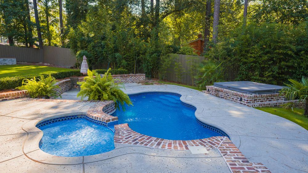 freeform fiberglass pool with tanning ledge and spa in a sloped backyard