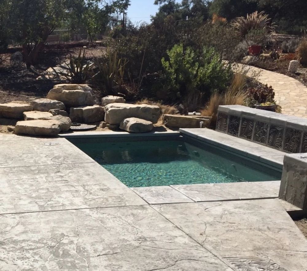 rectangular shaped pool with concrete deck and large boulders