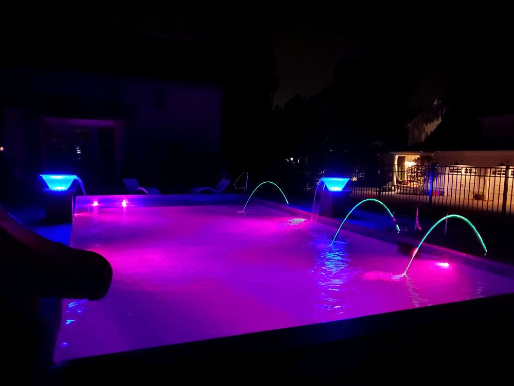 nighttime view of a pool with three streams of water flowing into pool and magenta lights illuminating pool surface