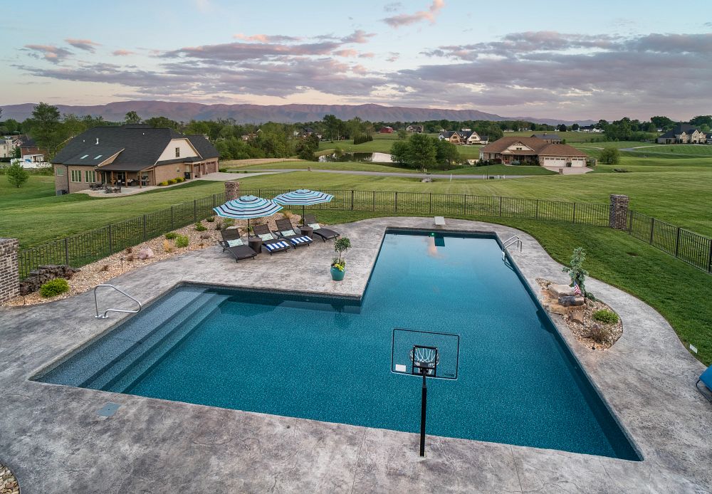 L-Shaped vinyl liner pool with basketball hoop and diving board in large, grassy backyard