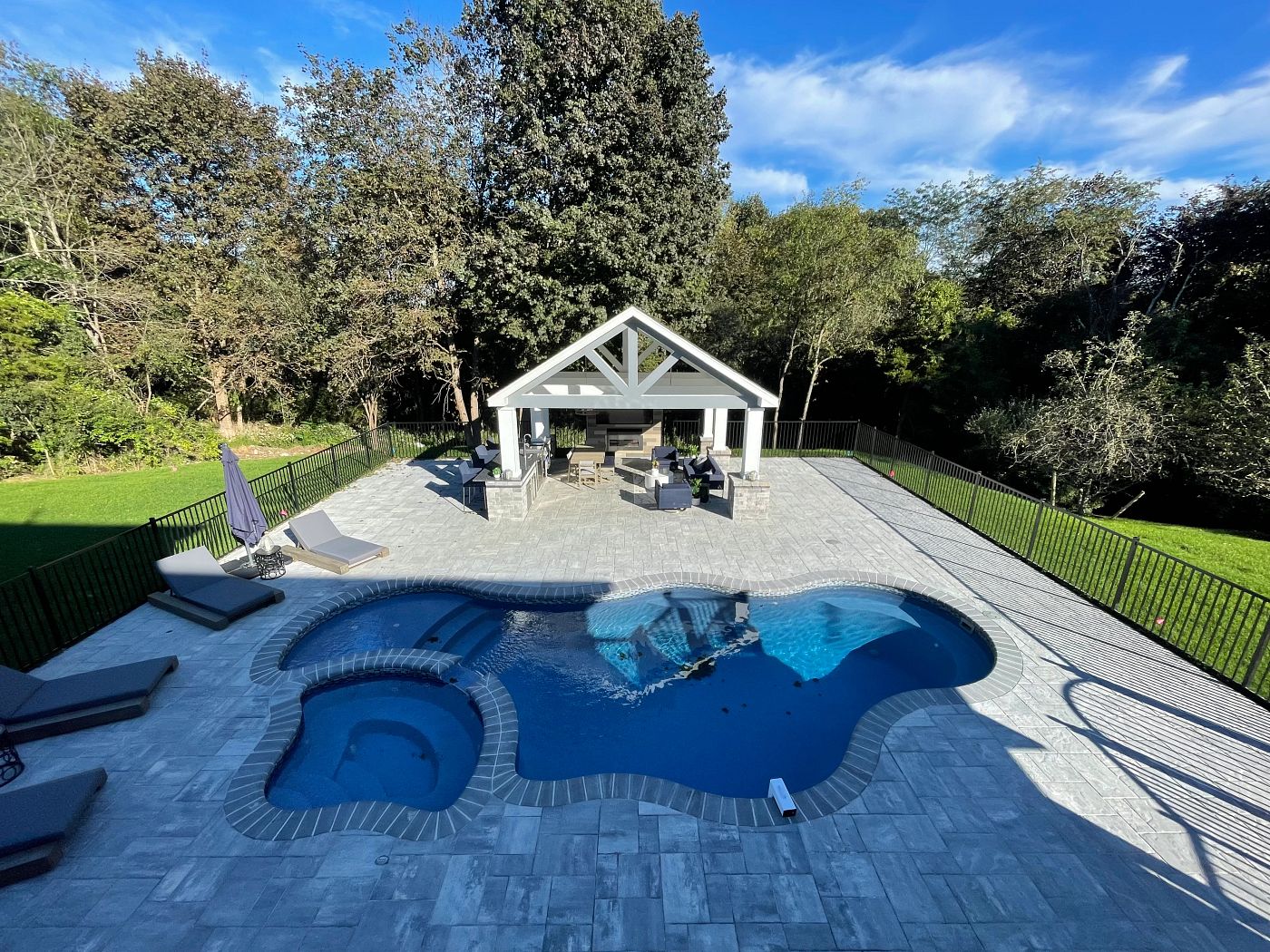 large fiberglass pool in fenced backyard with a gazebo