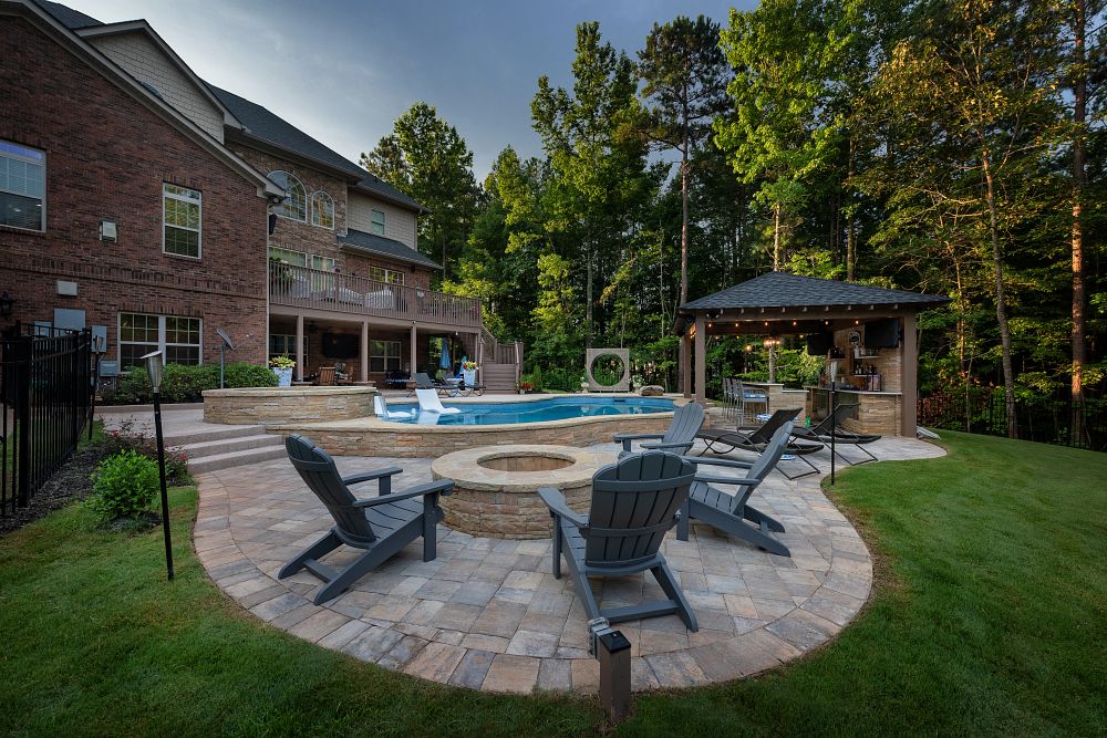 pool and spa on stone patio with a firepit surrounded by 4 adirondack chairs