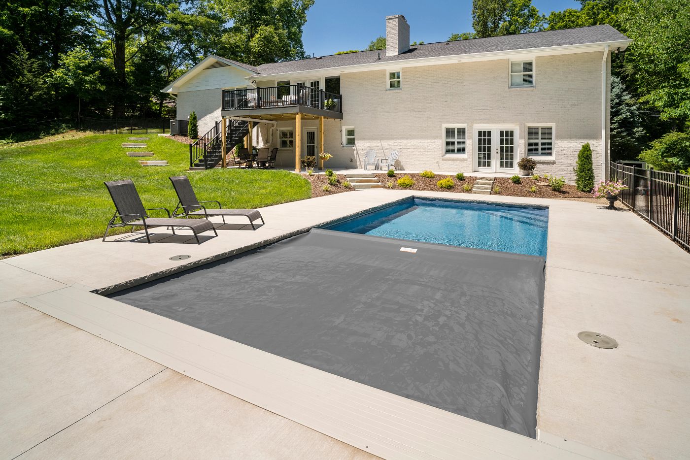 Fiberglass pool with automatic safety cover in a sloped Alabama backyard