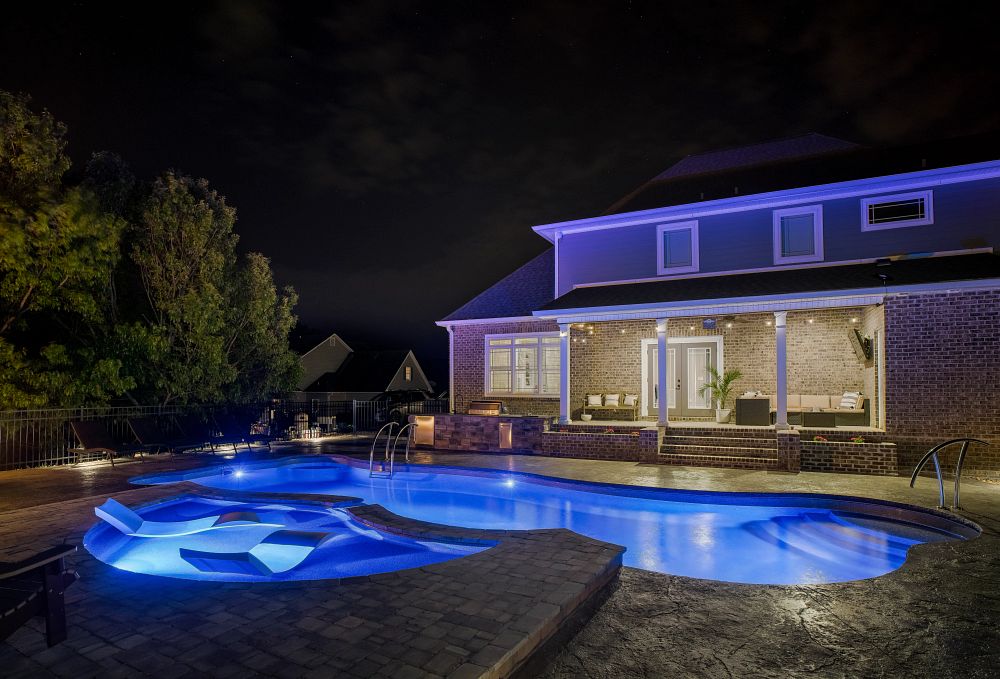 fiberglass pool at night with LED lights and tanning ledge in southern backyard