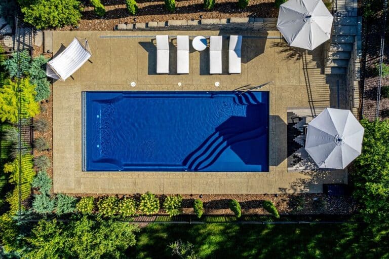 rectangular fiberglass pool surrounded by lounge chairs and umbrellas in southern backyard