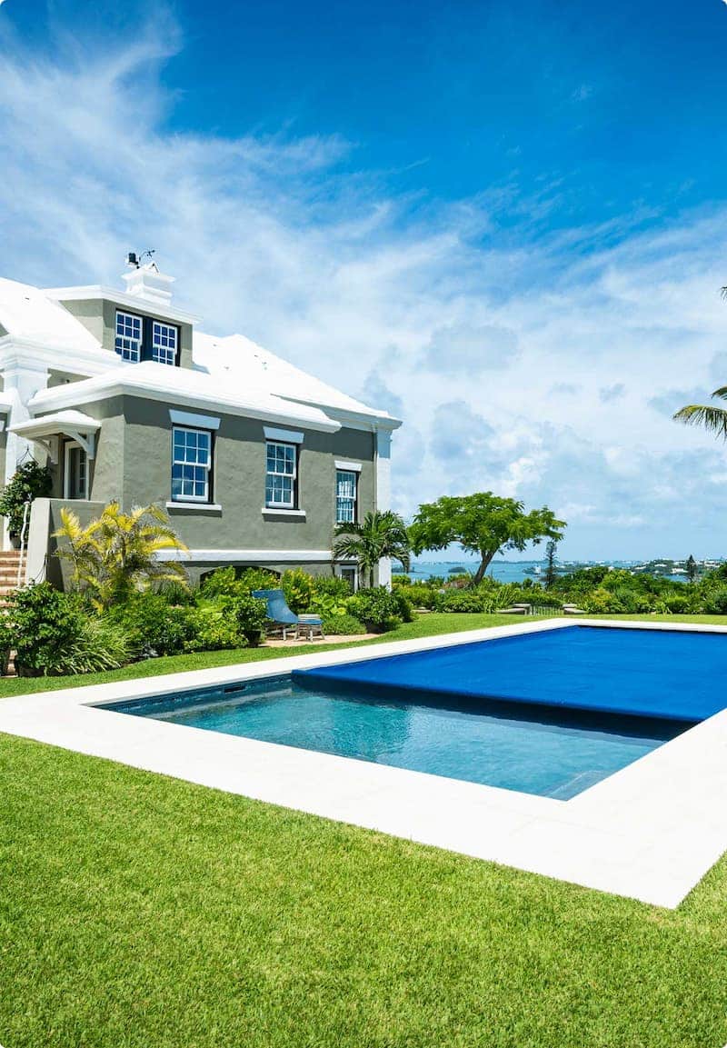 Automatic pool cover shown mid-roll over a rectangular pool, in a sunny residential backyard setting with palm trees.