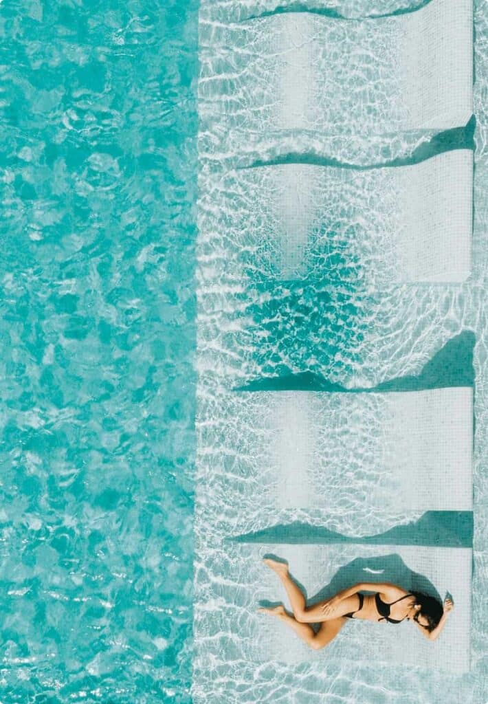 Woman relaxing on a tanning ledge in a pool under sunny skies.