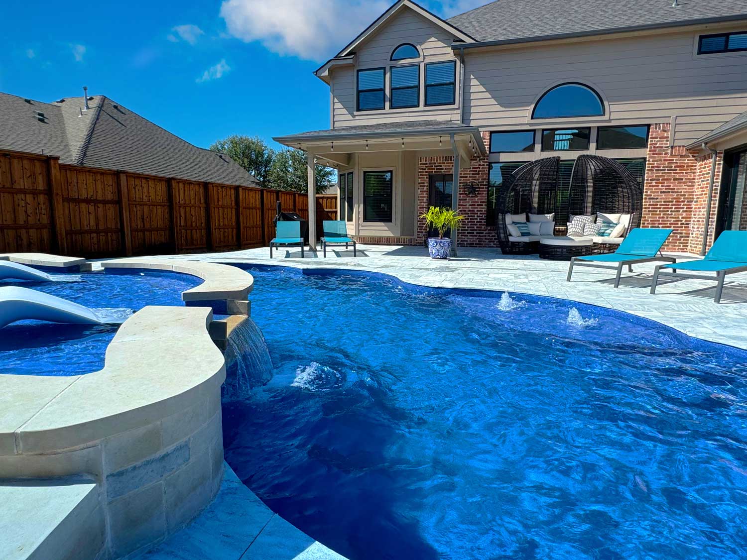 Vibrant vinyl liner pool in a residential backyard, bordered by lounge chairs and a brick home.