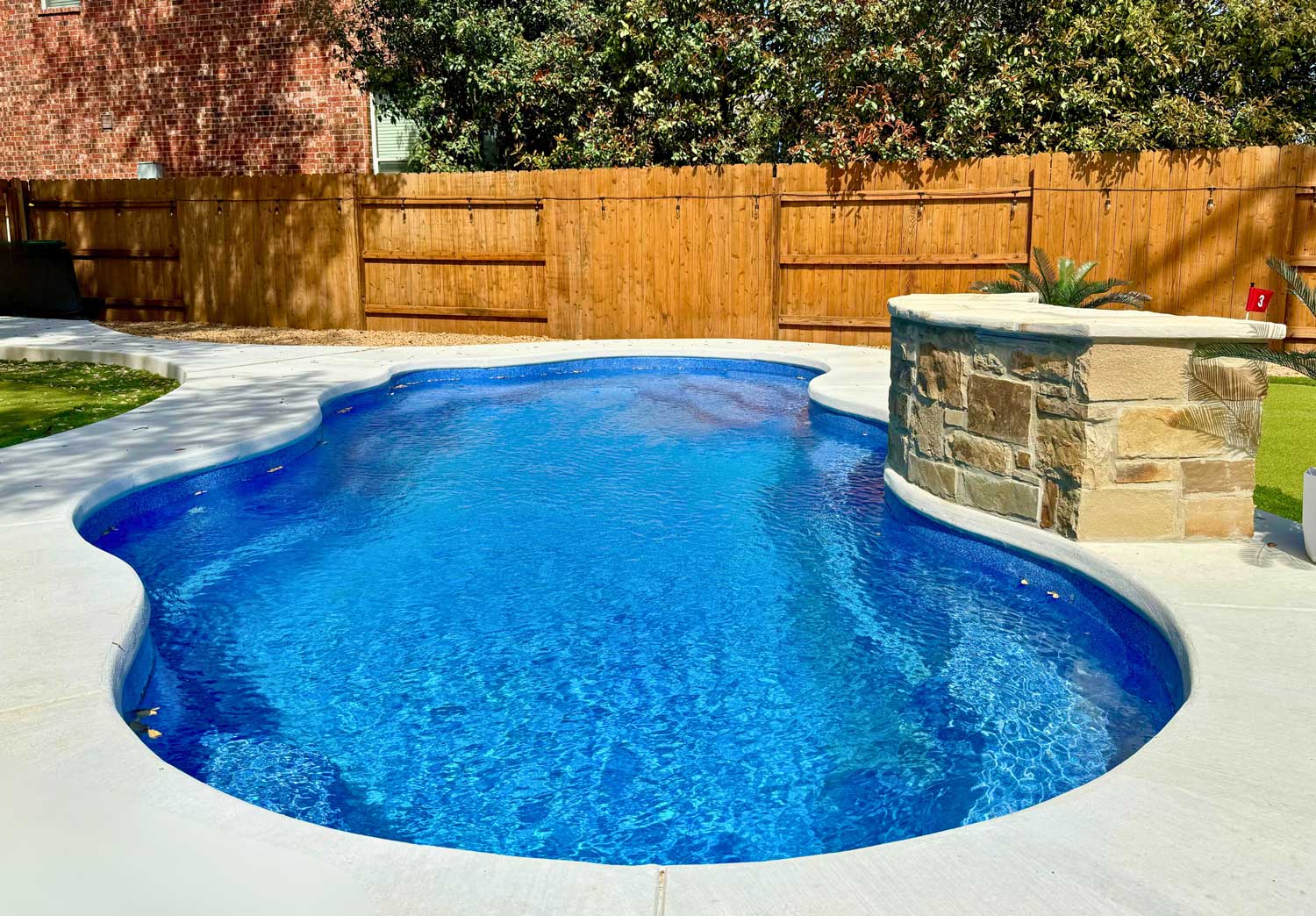 Freeform fiberglass pool with curved edges and built-in stone spillover feature in a private fenced yard.