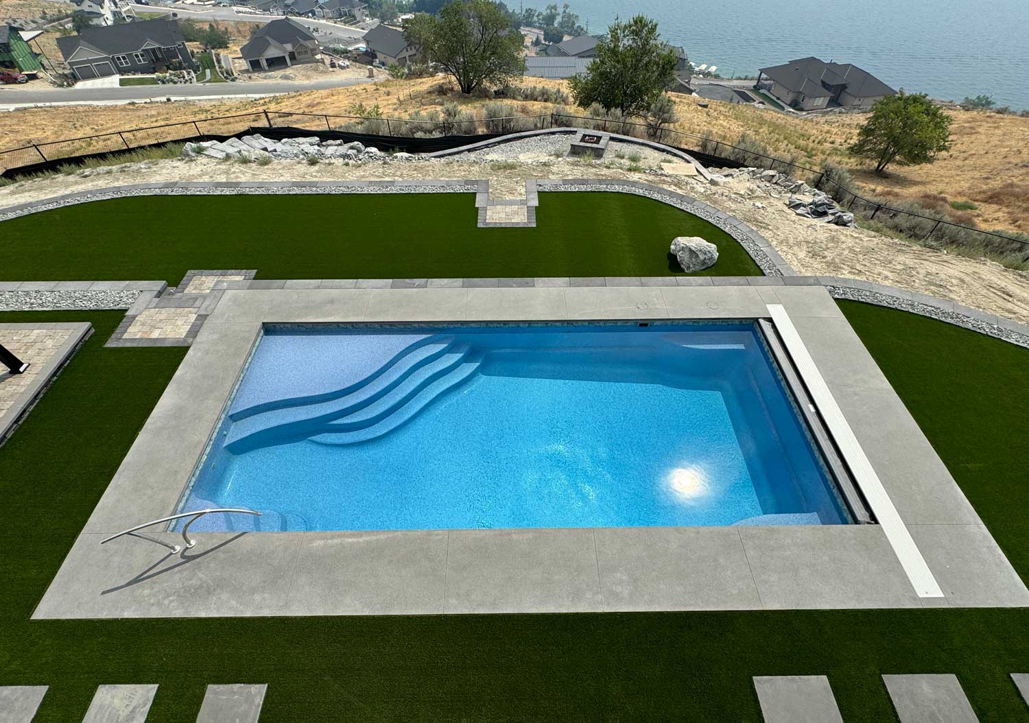 Rectangular fiberglass pool with clean lines and wide entry steps, set in a manicured backyard with open skies