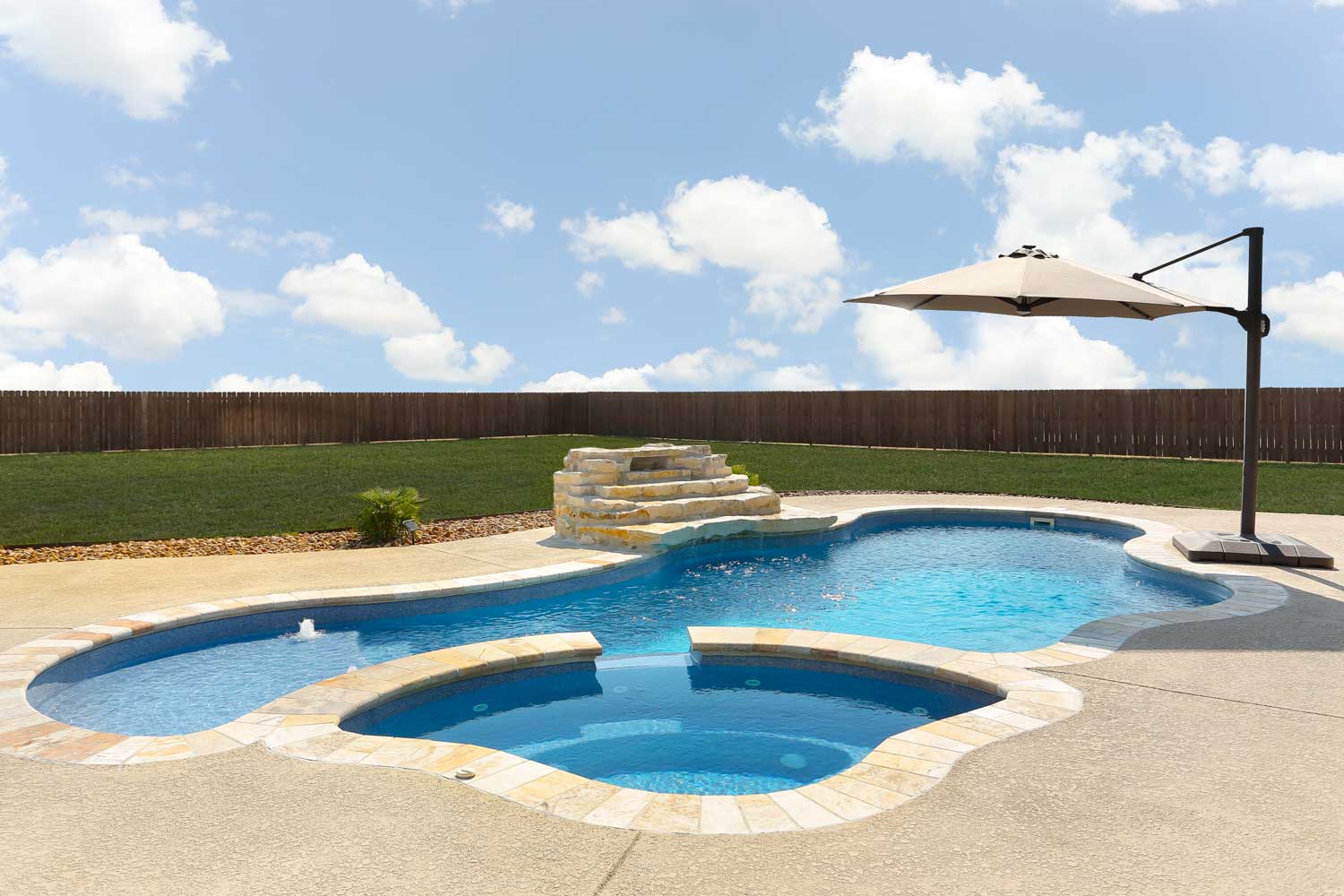 Freeform vinyl liner pool with an integrated spillover spa, surrounded by a smooth stone deck
