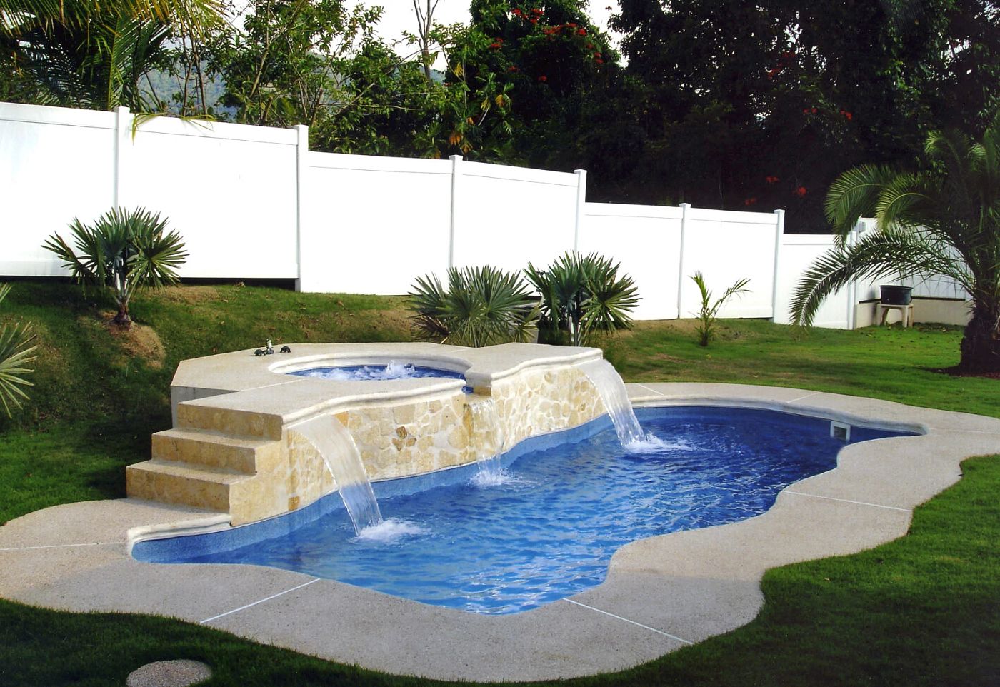 Freeform Latham Key West fiberglass pool with integrated elevated spa featuring natural rock coping and waterfall.