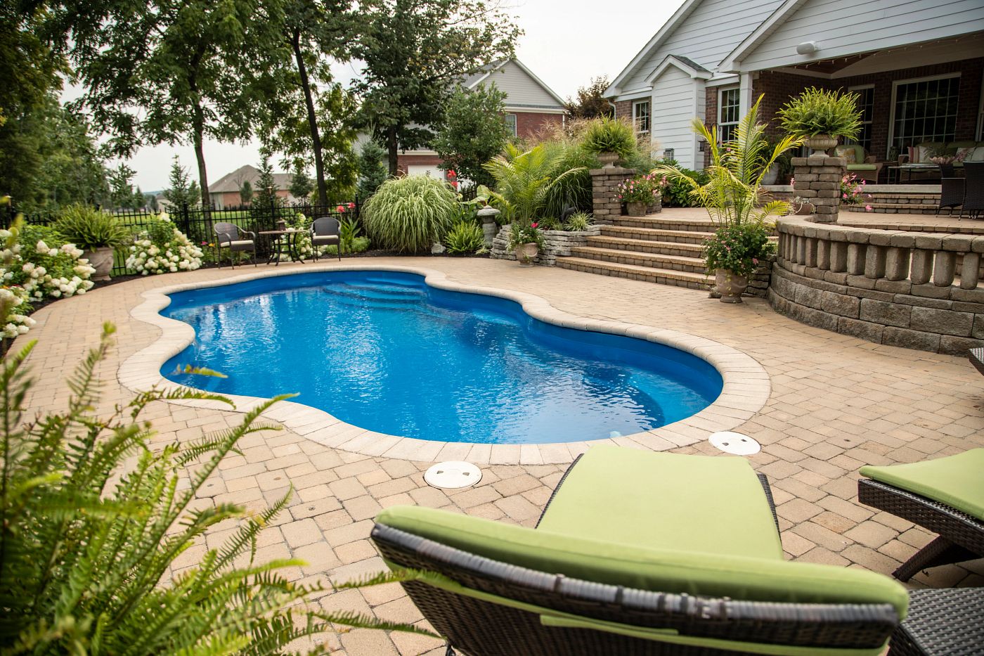 Freeform Laguna fiberglass pool surrounded by tan paver decking in a lush, private suburban backyard.