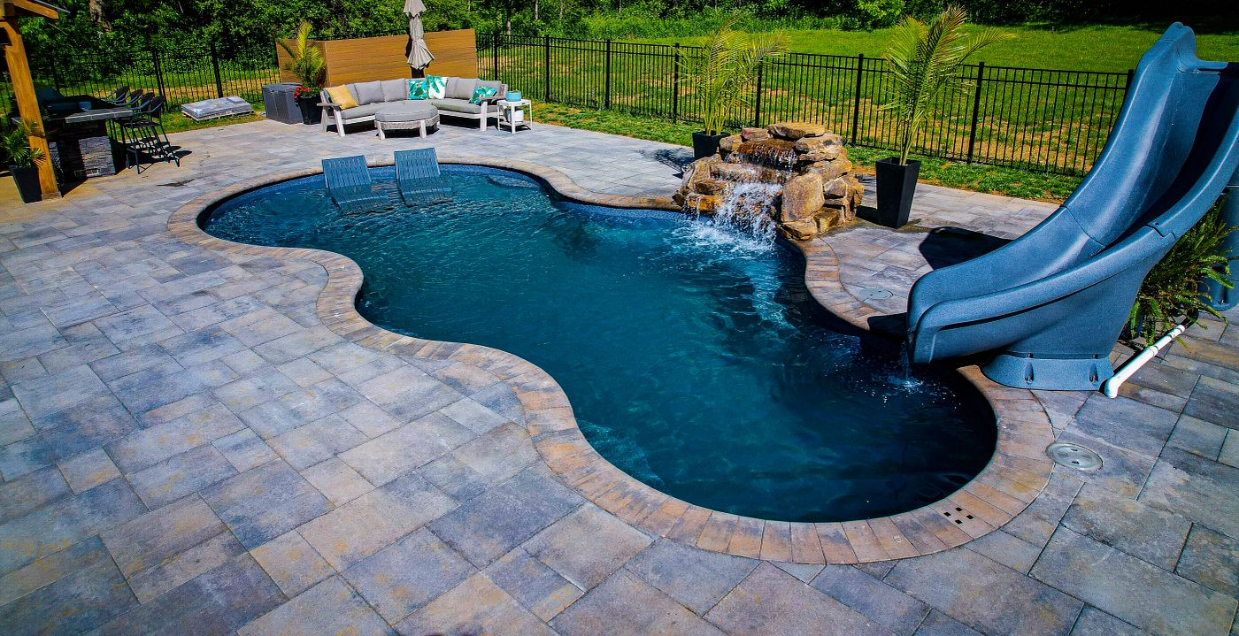 Freeform fiberglass pool with tanning ledge, built-in water feature, and slide.