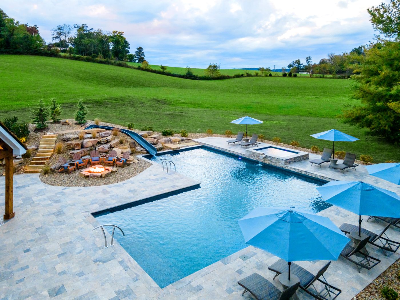 Large vinyl liner pool in a wide open, grassy setting featuring a spillover spa and water slide.