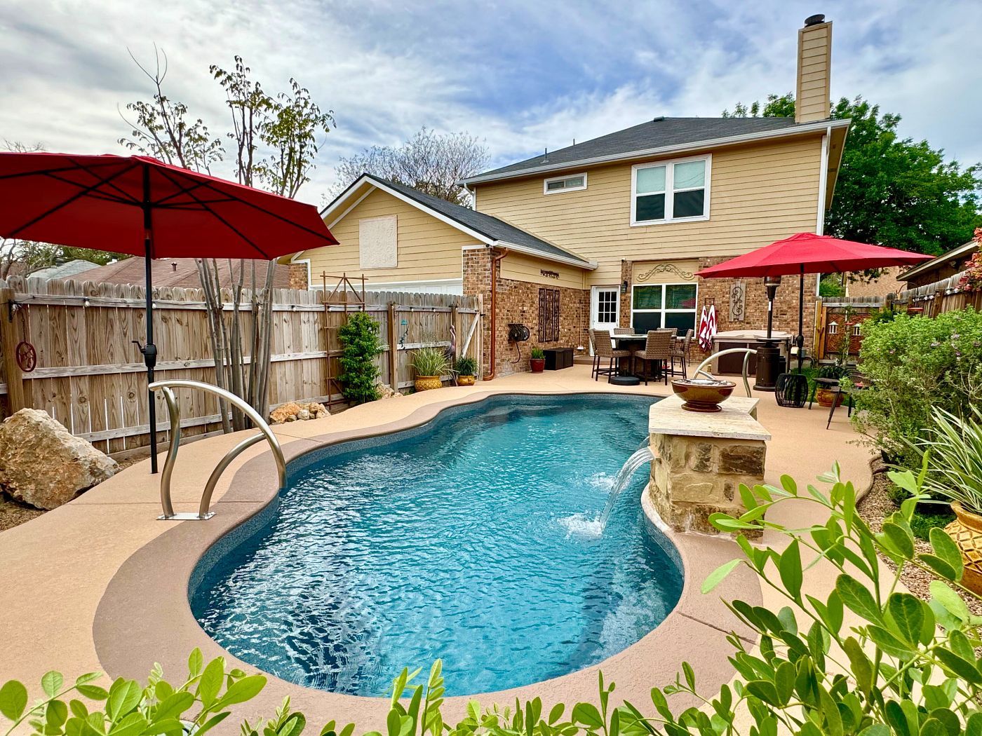 Freeform fiberglass pool with stone coping and landscaping in a suburban backyard.