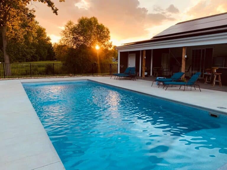 Backyard patio featuring a blue rectangular Latham fiberglass pool with a clear evening sunset view.