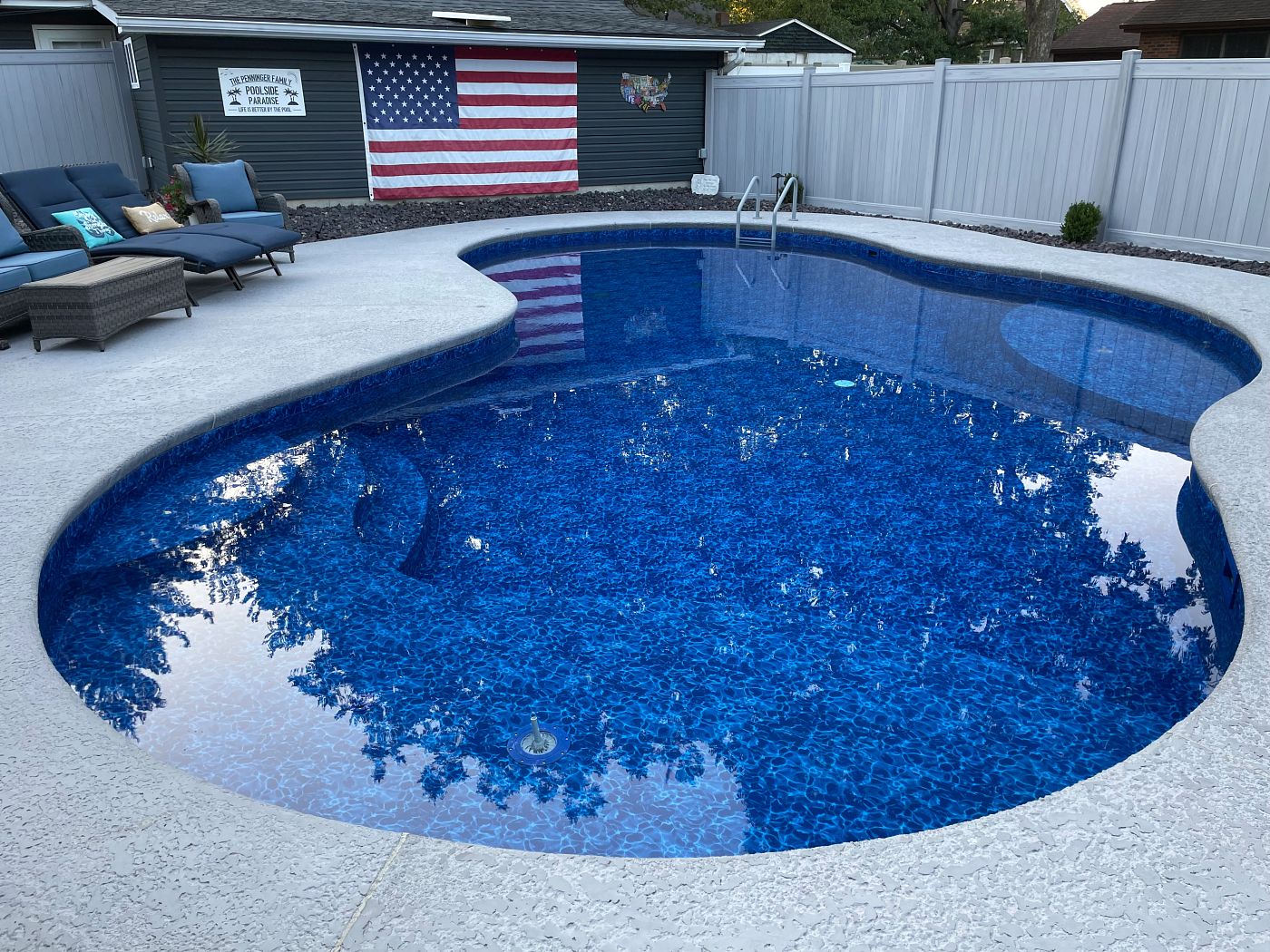 Large freeform inground vinyl liner pool with blue mosaic liner pattern and surrounding lounge seating.