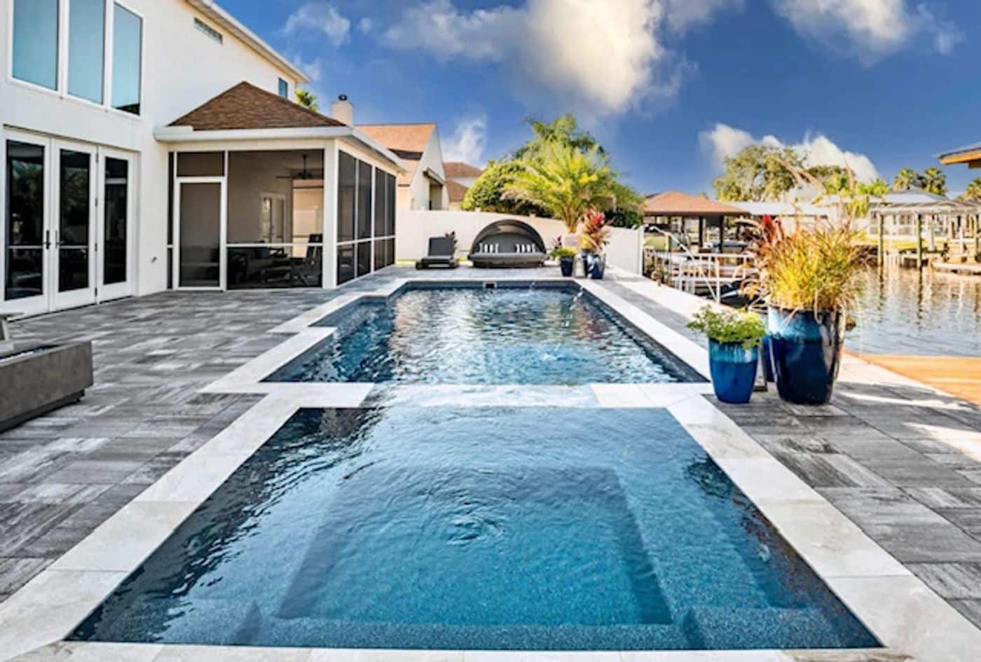 Rectangular fiberglass pool with integrated spa and a screened patio enclosure overlooking a waterfront view.