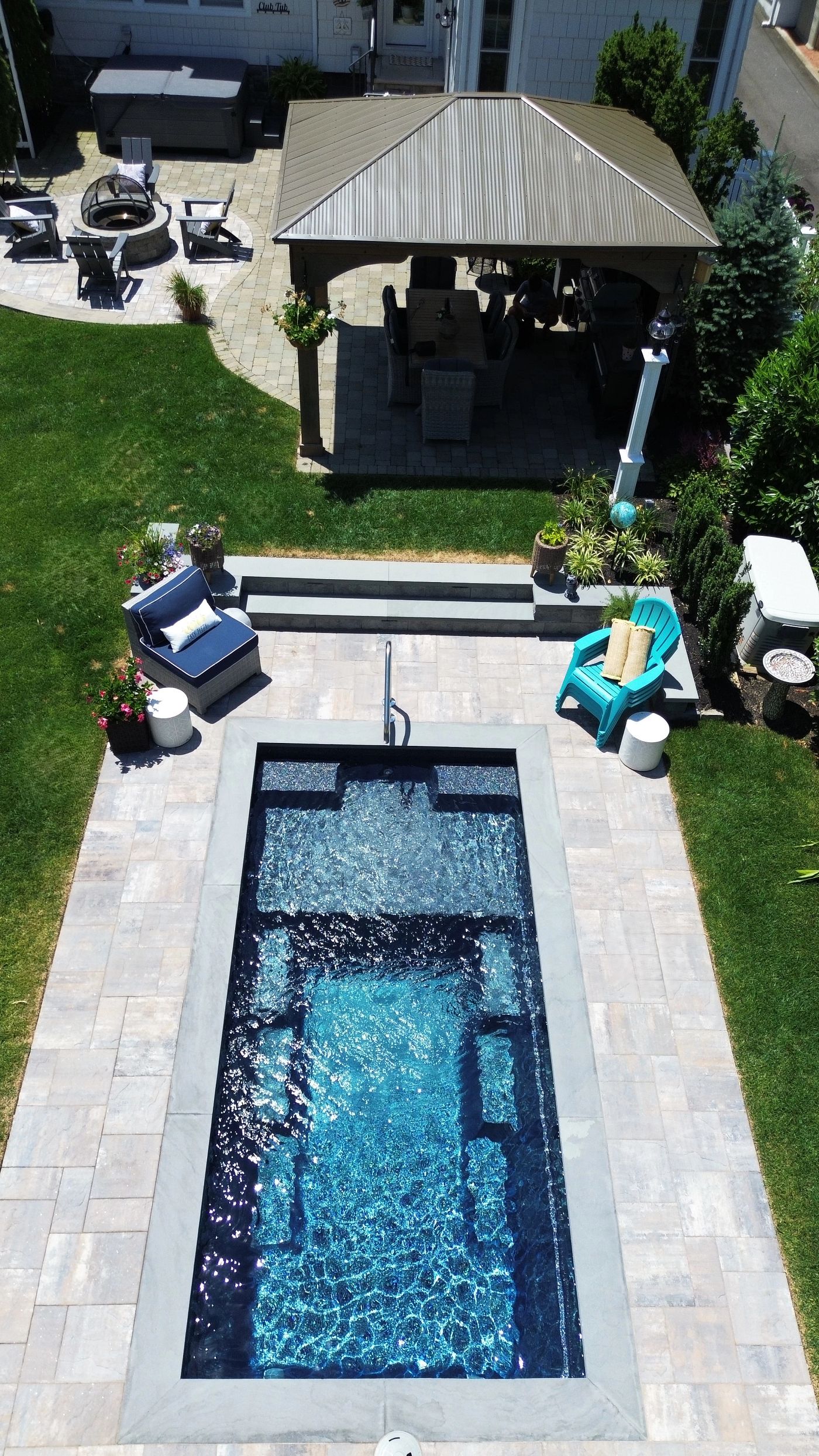Overhead view of a rectangular fiberglass plunge pool with light patio pavers in a narrow backyard.