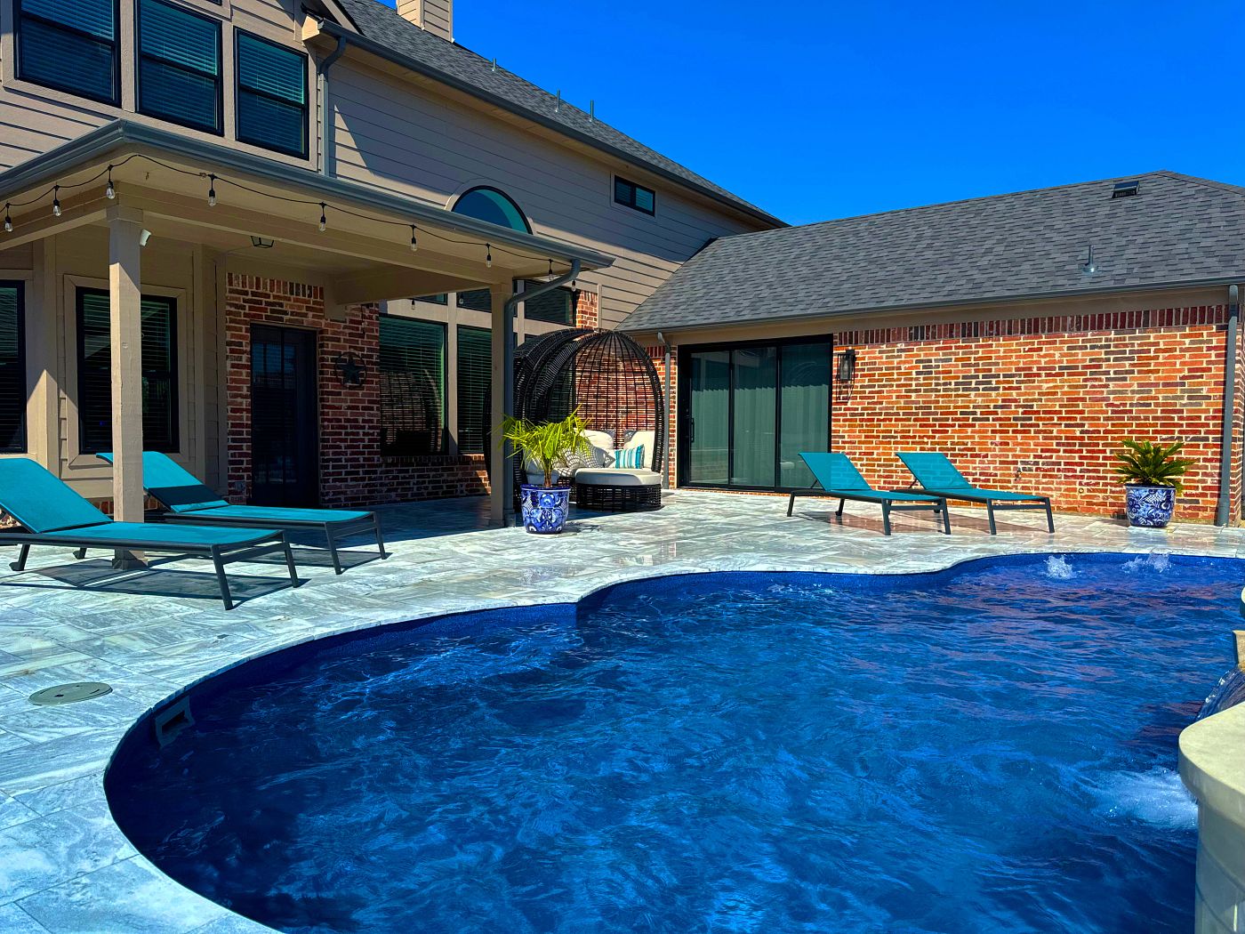 Backyard fiberglass pool with curved edges, stone patio, and lounge chairs.
