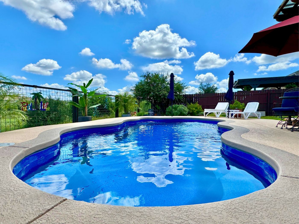 Sparkling blue fiberglass pool with lounge chairs and umbrellas under a bright Houston sky.