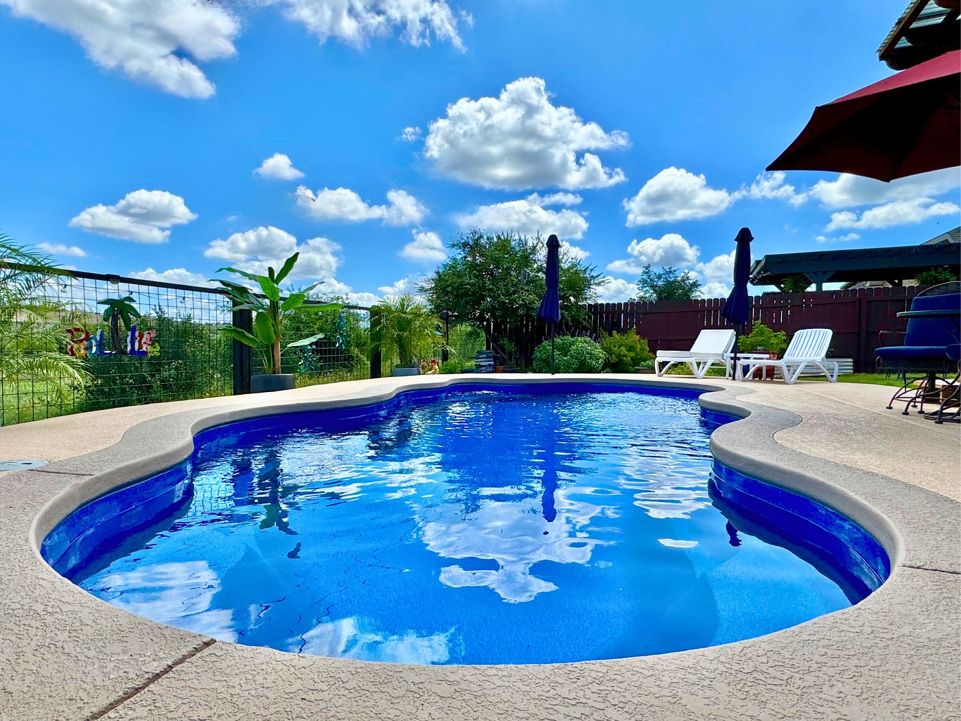 Sparkling blue fiberglass pool with lounge chairs and umbrellas under a bright Houston sky.