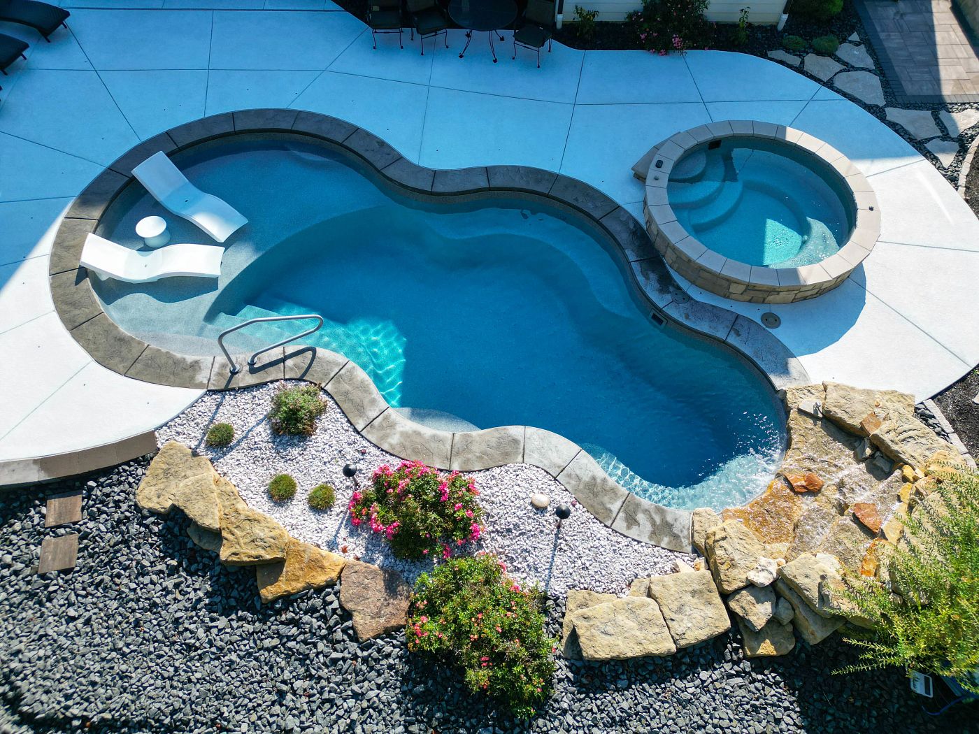 Freeform fiberglass pool and elevated spa with natural stone coping and dry, desert-friendly landscaping.