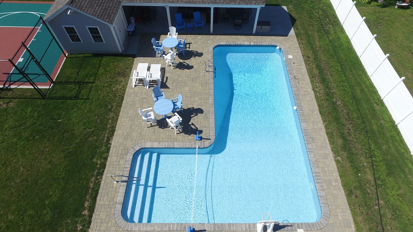Aerial view of a large L-shaped vinyl liner pool featuring wide corner steps and a surrounding sun deck.