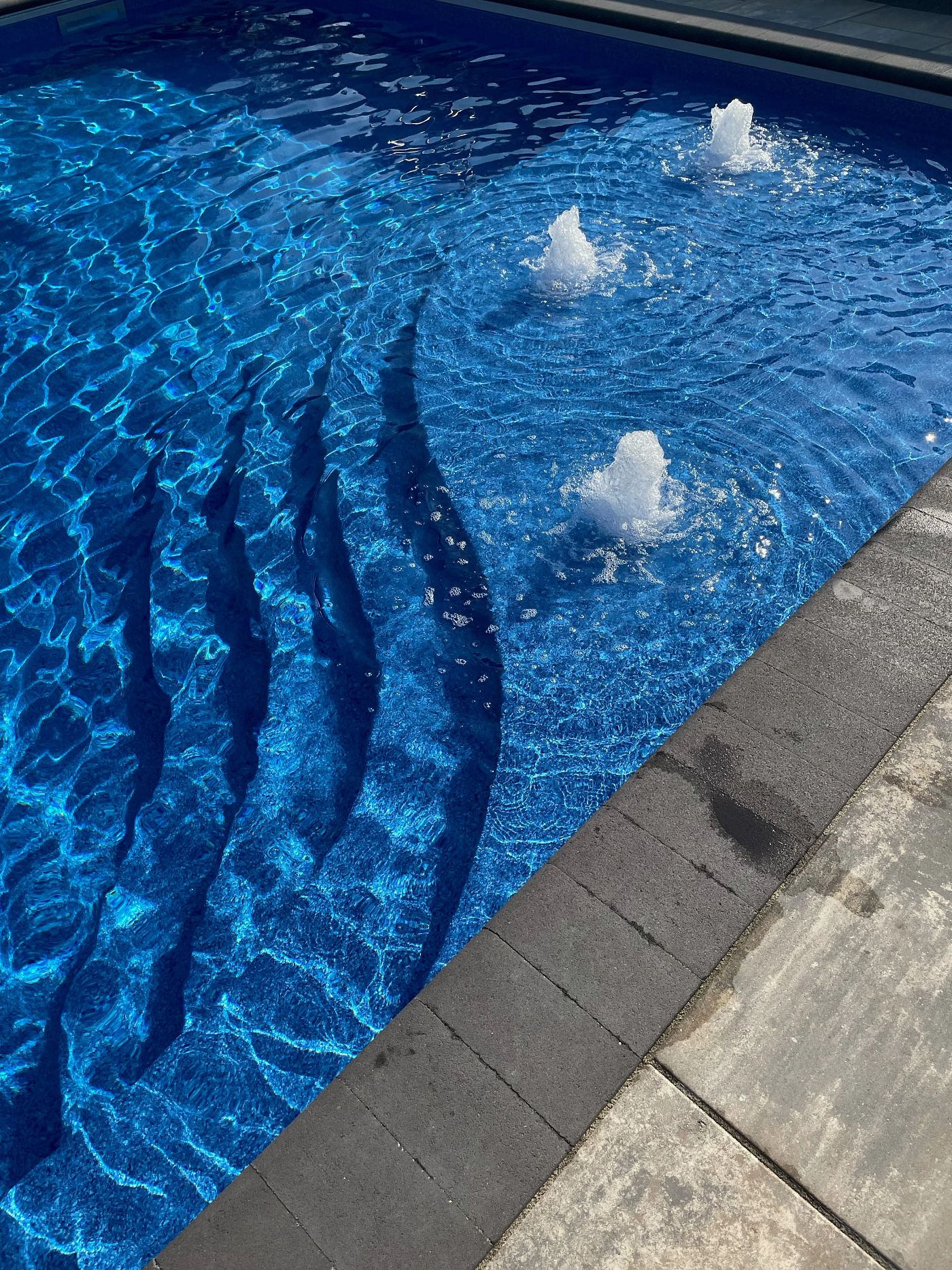 Rectangular vinyl liner pool in deep blue with auto safety cover and stone terrace.