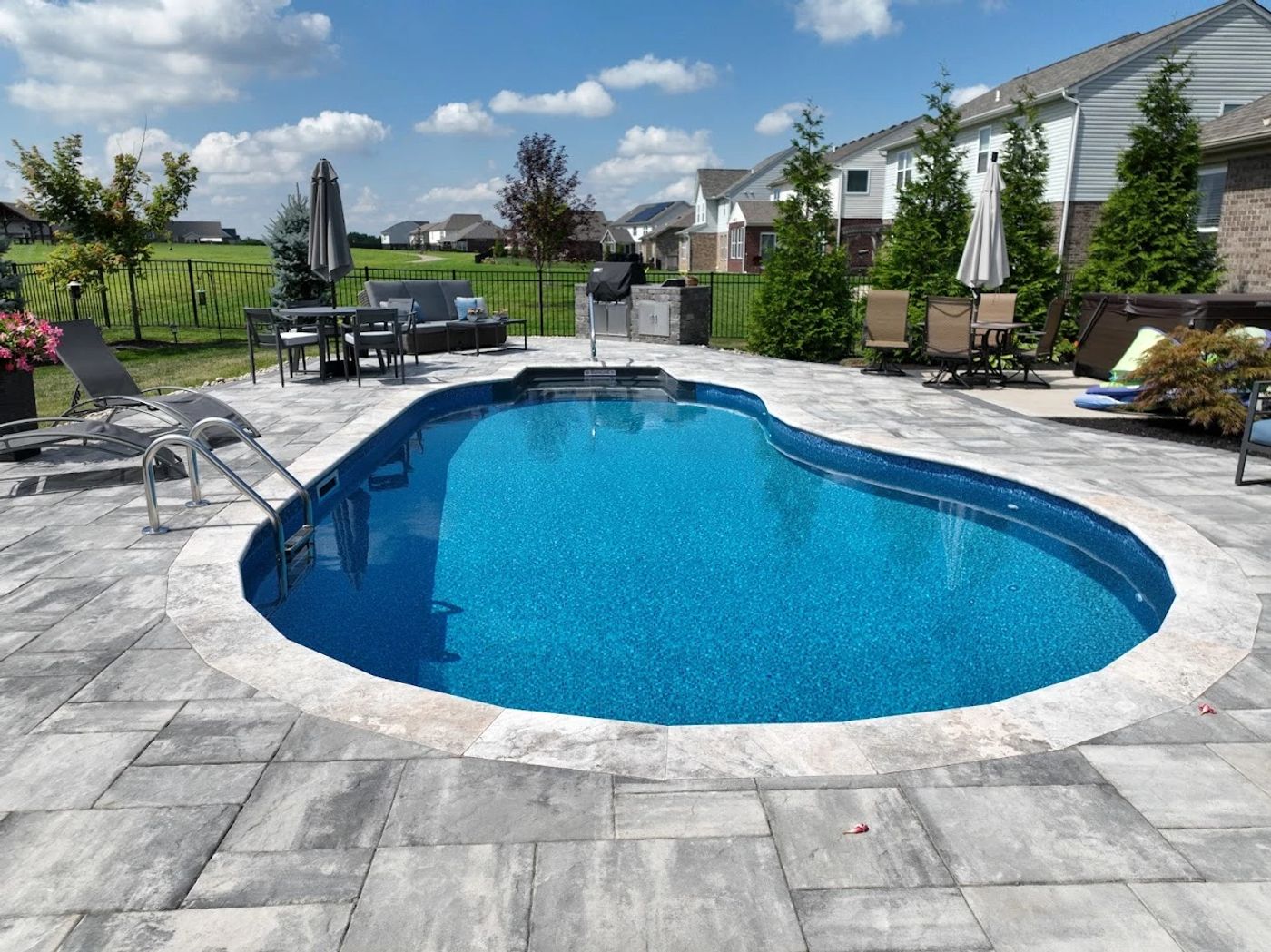 Wide kidney-shaped inground vinyl liner pool featuring a built-in full-width tanning ledge and dark blue tile trim.